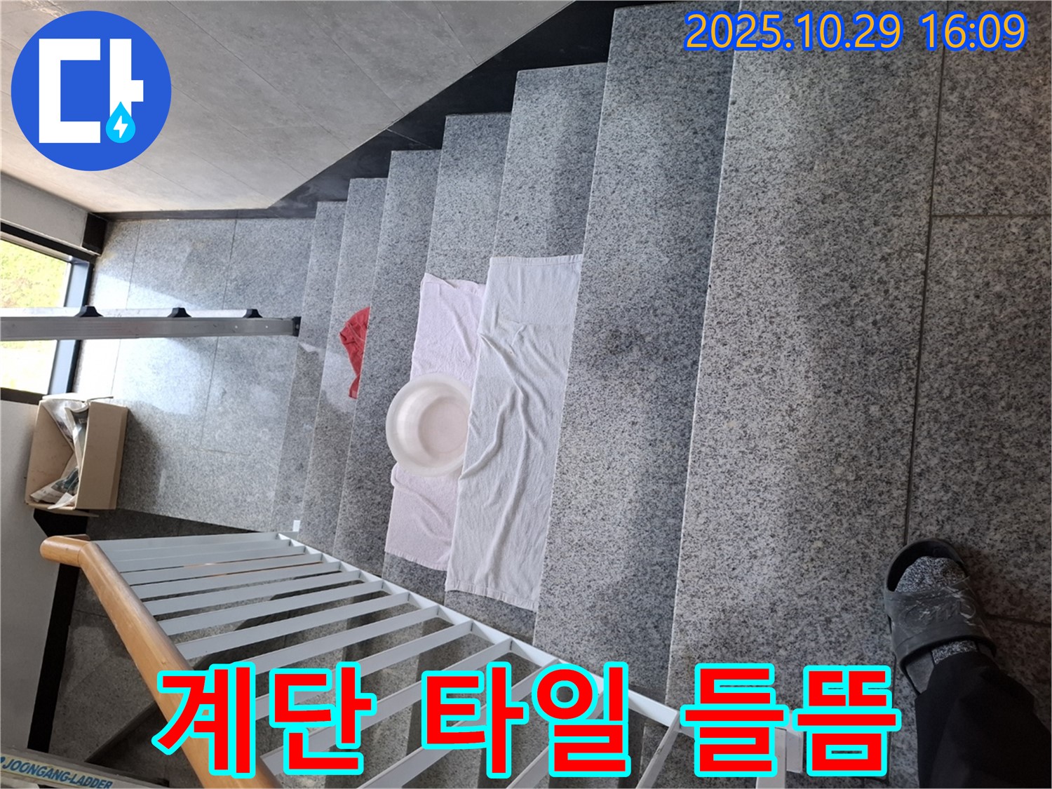 계단에 놓인 대야와 수건 - 타일 들뜸으로 인한 안전사고 위험을 경고합니다.