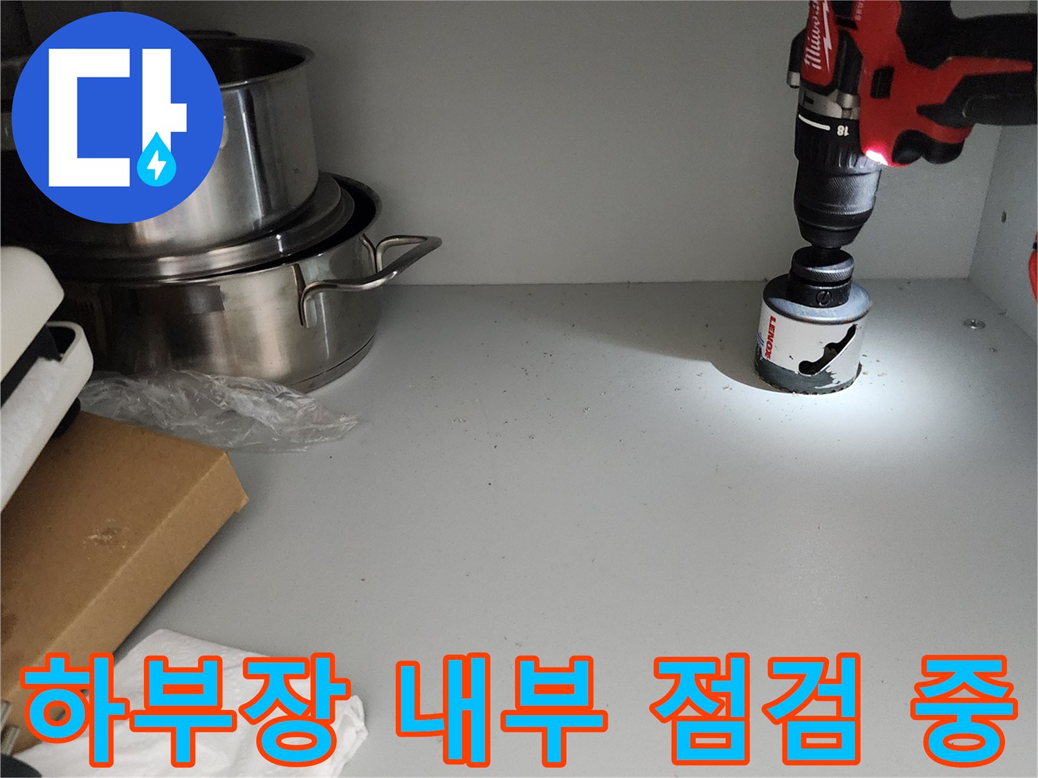 조명 장비를 사용하여 싱크대 하부장 구석을 비추는 엔지니어의 작업 모습