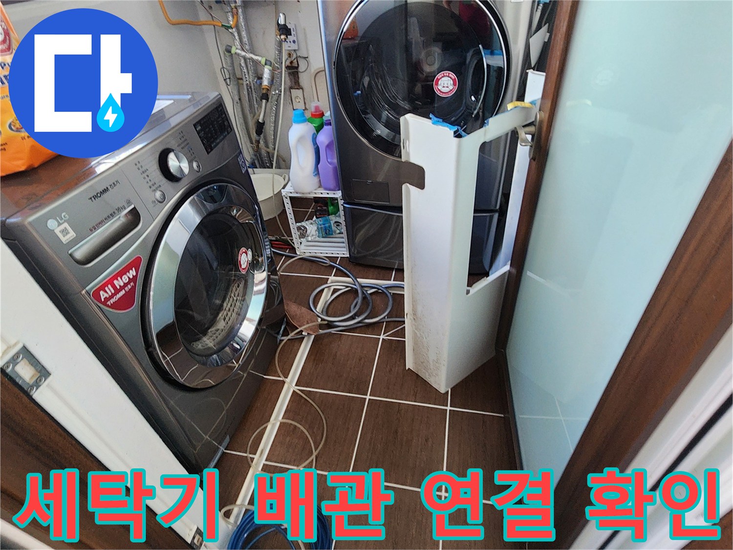 세탁실 내부의 드럼 세탁기와 건조기 하단 배관 연결 상태를 보여줍니다.