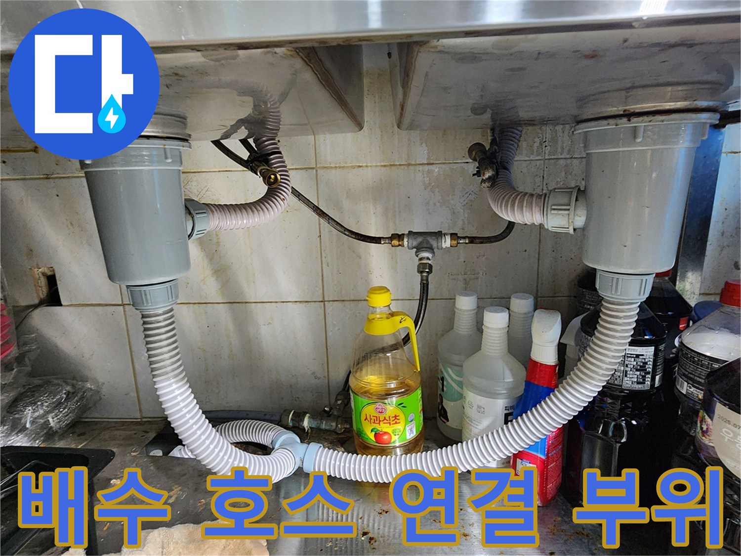 주방 배수 호스가 굴곡져 연결된 싱크대 하부 배관 모습