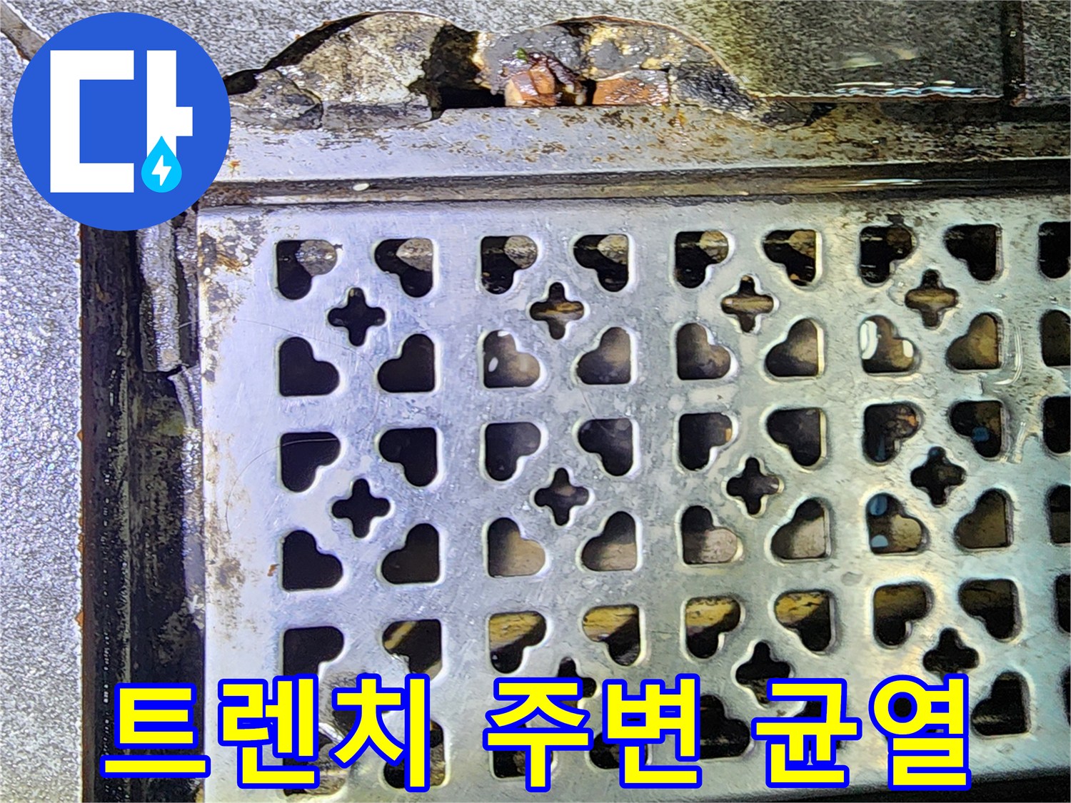 배수 트렌치 덮개 옆으로 드러난 깨진 콘크리트와 습한 바닥