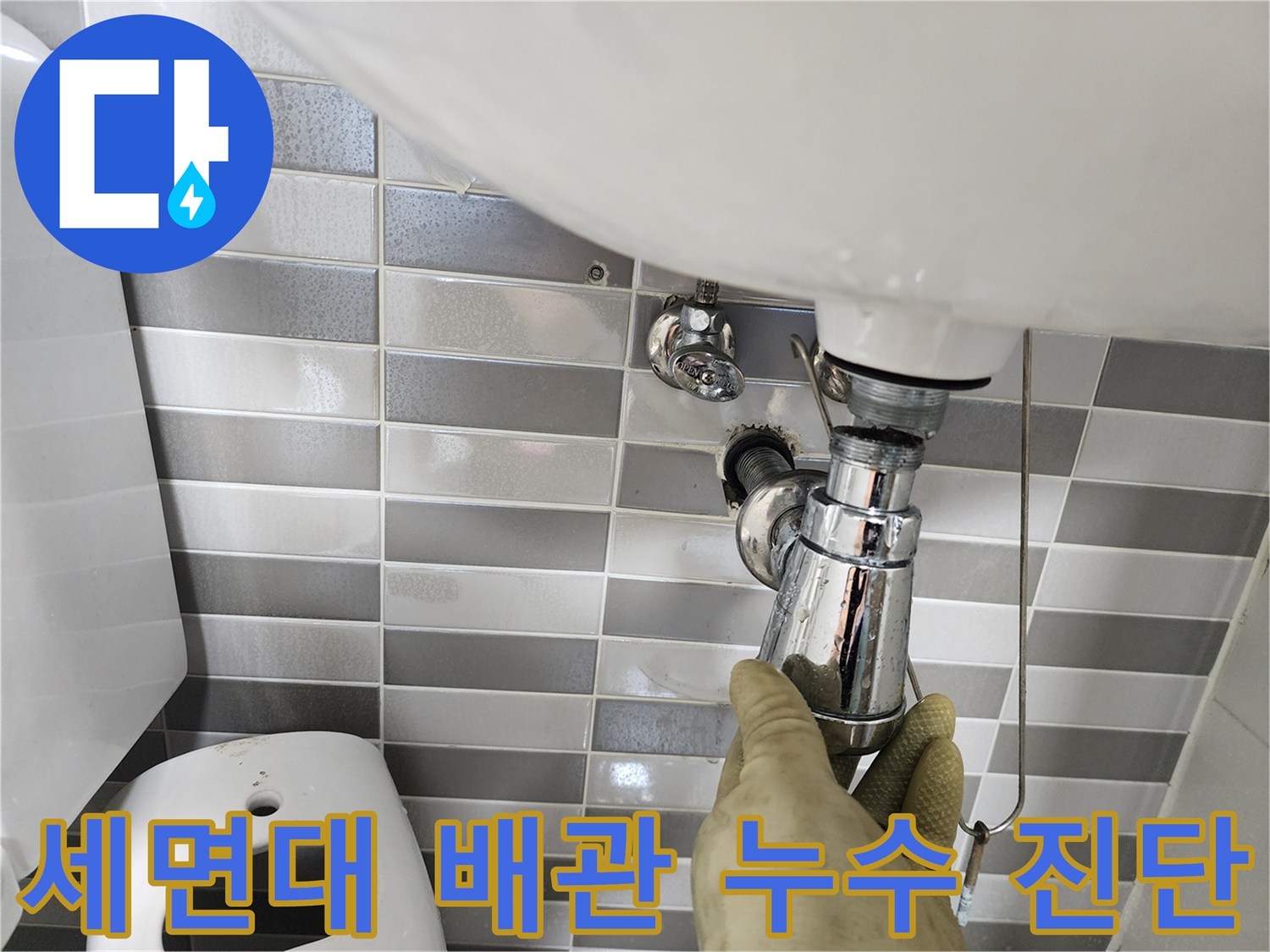 엔지니어가 세면대 하부의 금속 배관 연결 부위를 손으로 만지며 점검하는 장면입니다.