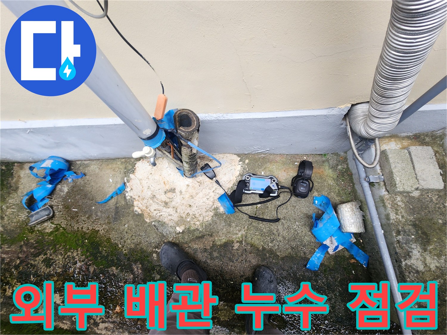건물 외벽 하단에 노출된 파손된 배관과 누수 탐지 장비 모습