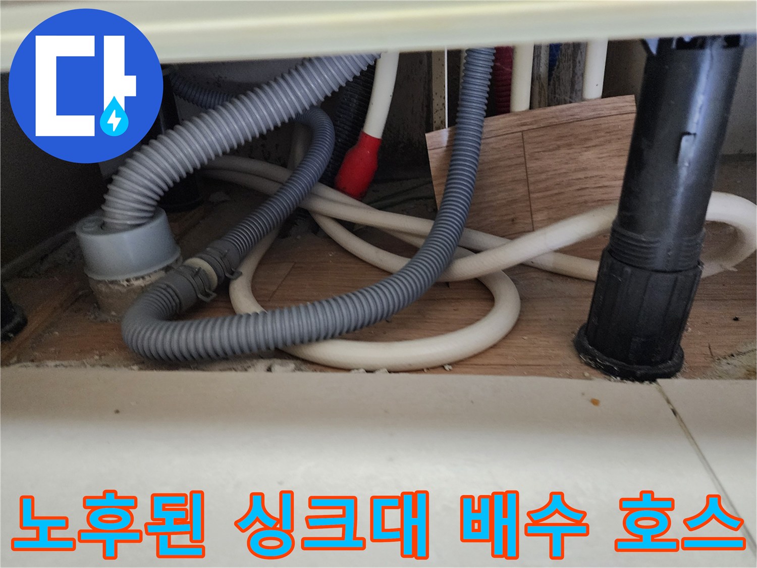 싱크대 아래 꼬여 있는 회색 주름관과 검은색 배관 연결부