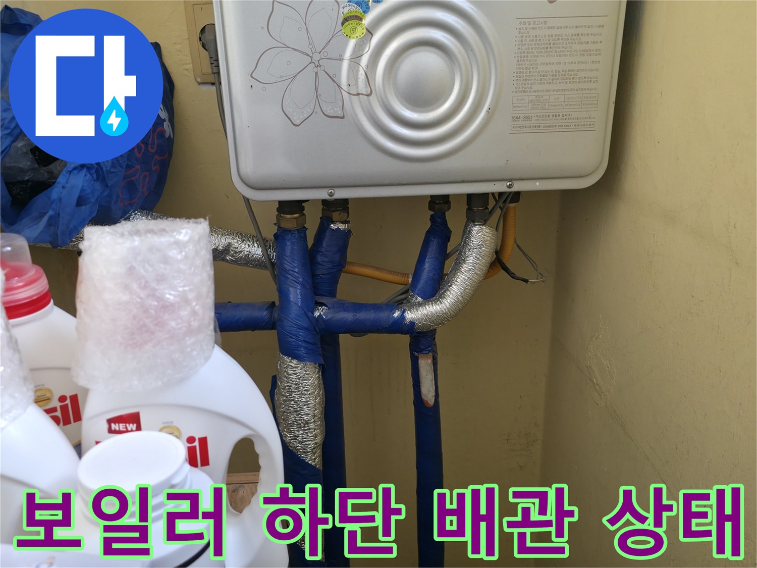 보일러 아래 연결된 파란색 배관과 보온재 마감 상태를 보여주는 사진입니다.