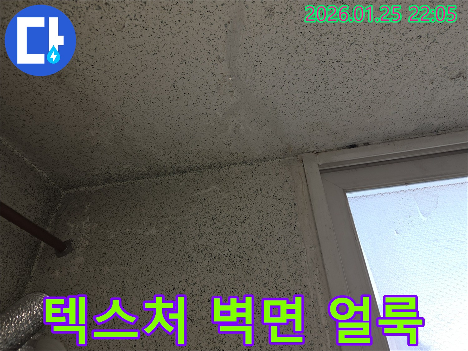 텍스처 처리된 벽면과 천장에 나타난 누수로 인한 어두운 얼룩-물이 스며든 흔적을 보여주는 사진