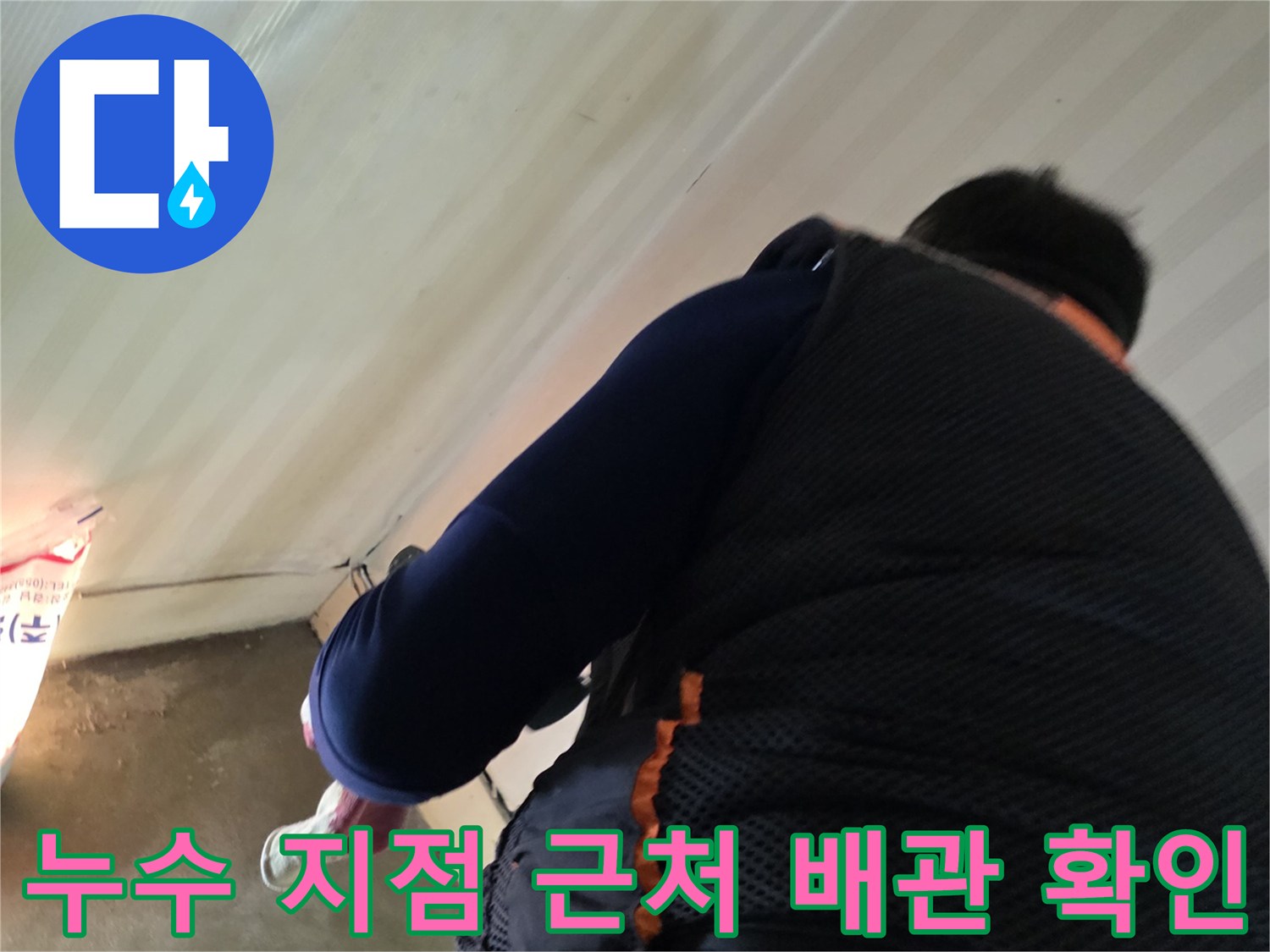작업자가 보일러실 바닥의 배관 연결 부위를 면밀히 조사하고 있습니다.