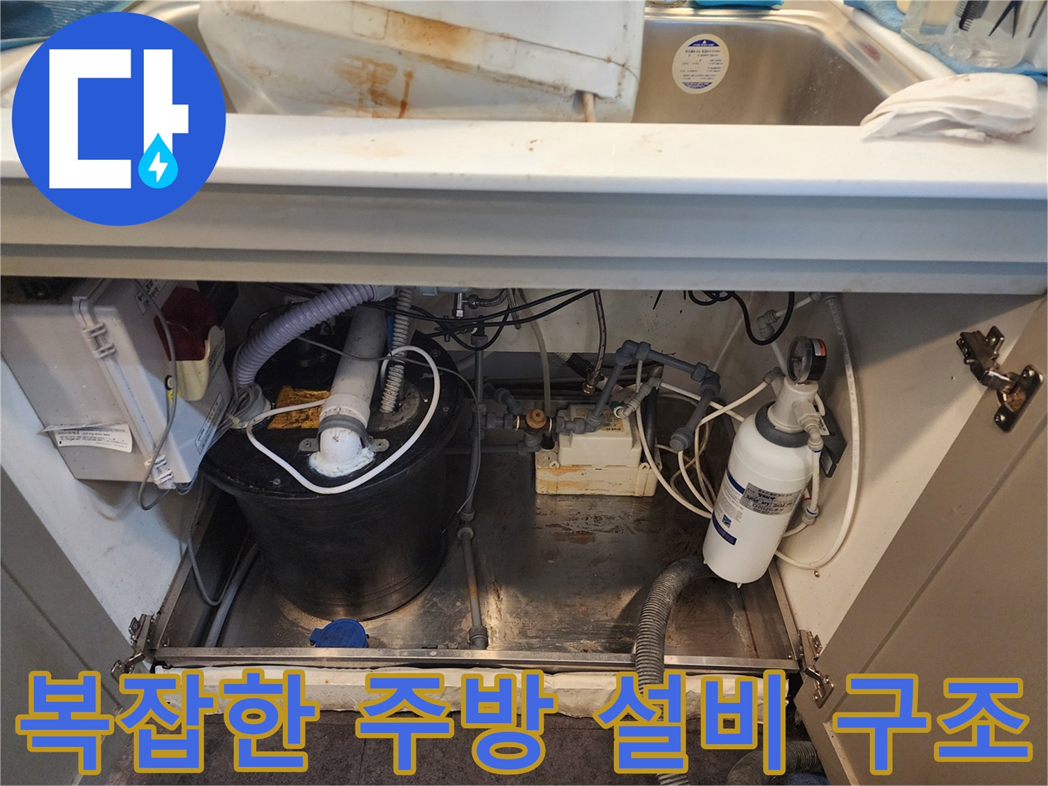 주방 싱크대 아래 온수기와 밸브 및 연결 호스가 복잡하게 배치된 모습