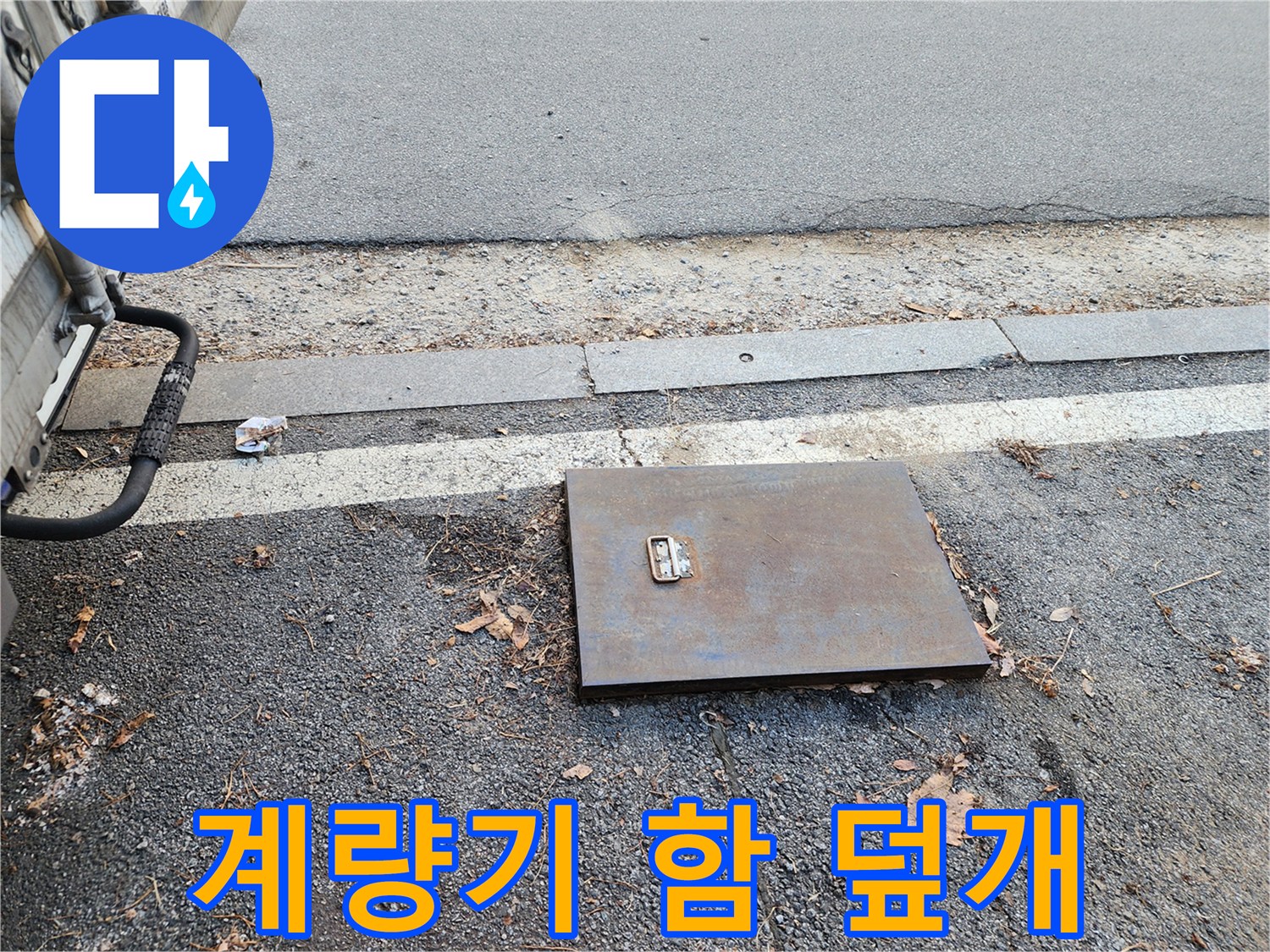도로 경계석 아래 설치된 사각형 형태의 금속제 계기함 덮개입니다.