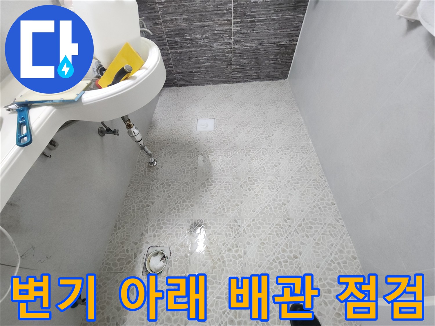 변기를 들어낸 후 노출된 하얀색 타일 바닥과 배수구 부위
