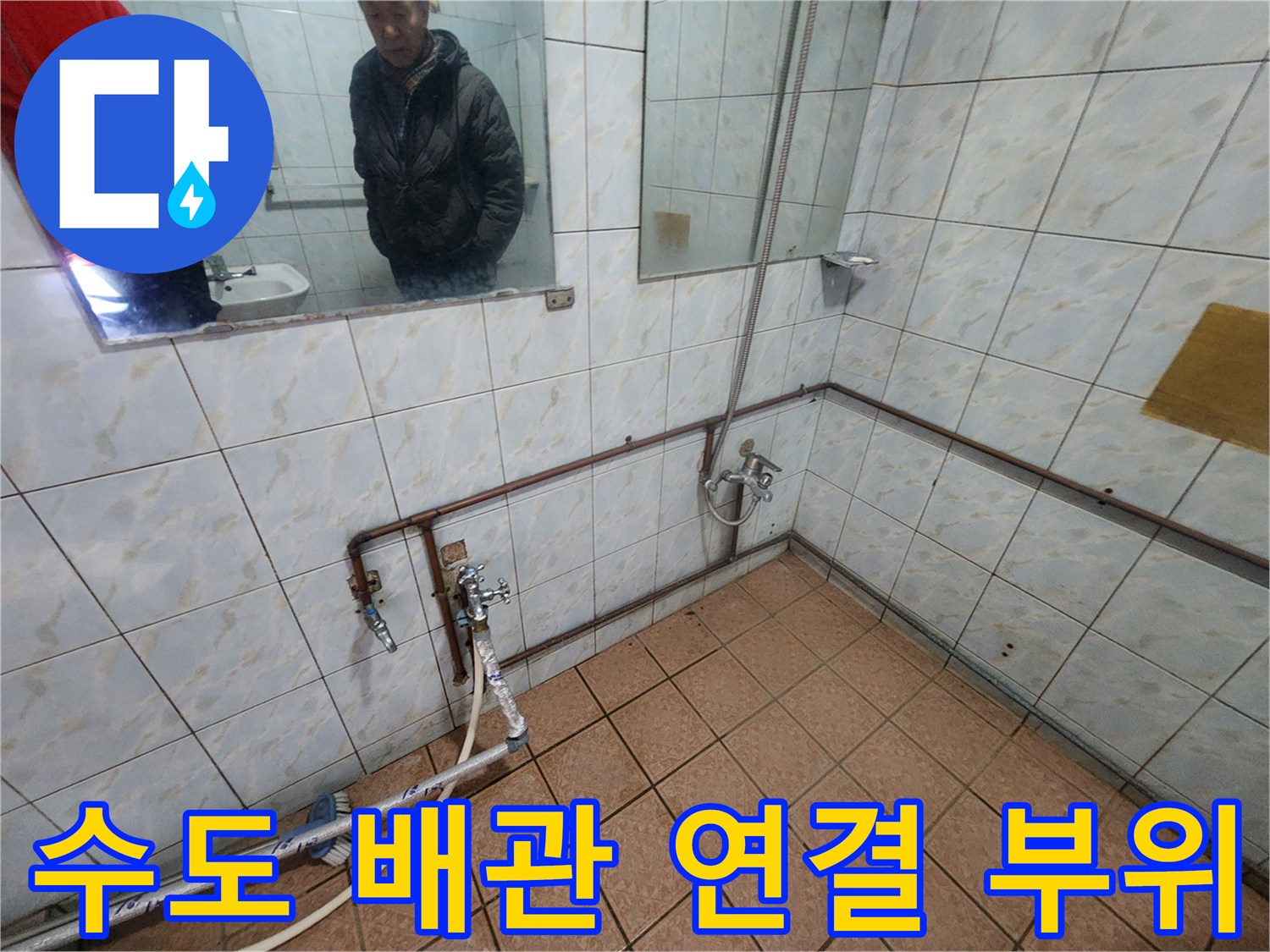 화장실 벽면 타일에 고정된 금속 수도 배관과 밸브 형태의 부품