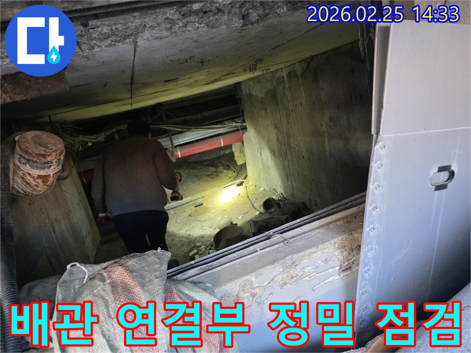 누수 전문 엔지니어가-어둡고 좁은 공간에서-손전등을 비춰가며-배관 연결부의 누수 여부를-정밀하게 점검하는 모습입니다.