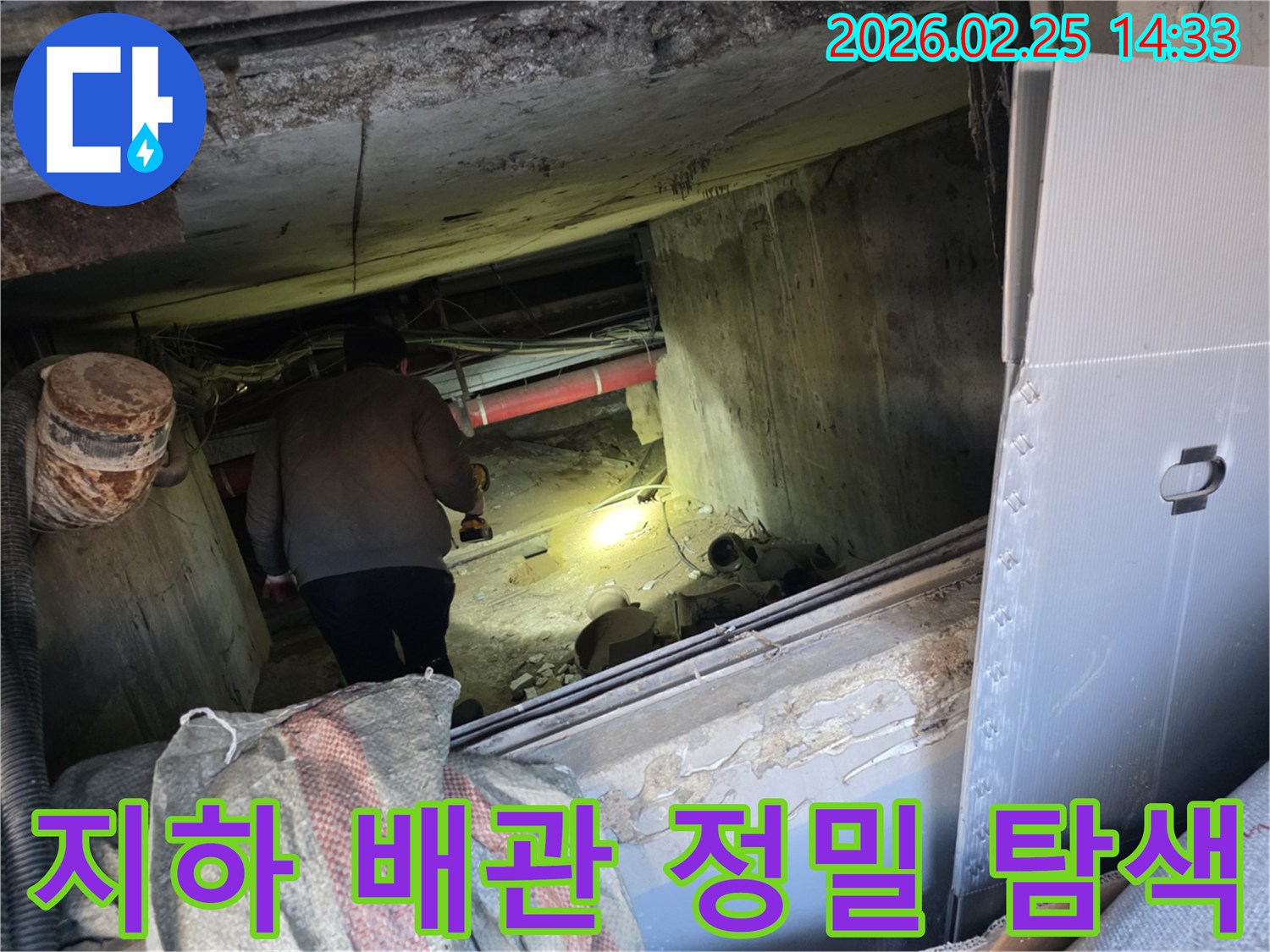누수 전문 엔지니어가-어둡고 좁은 지하 공간에서-손전등을 비춰가며-배관의 누수 지점을-정밀하게 탐색하는 모습입니다.