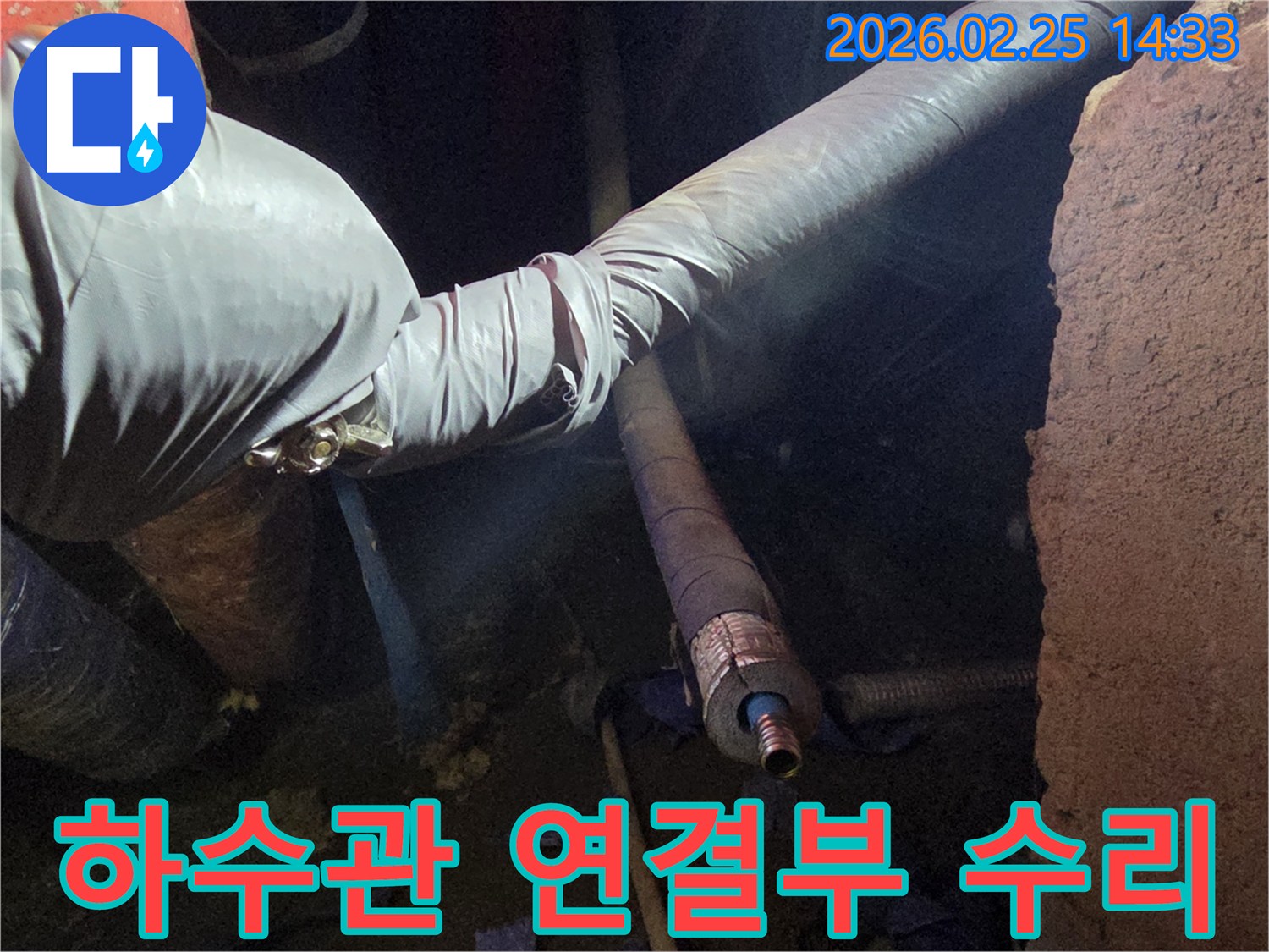 어둡고 좁은 공간에서-장갑을 낀 손이-베란다 하수관의-손상된 연결 부위를-세심하게 수리하는-모습을 담고 있습니다
