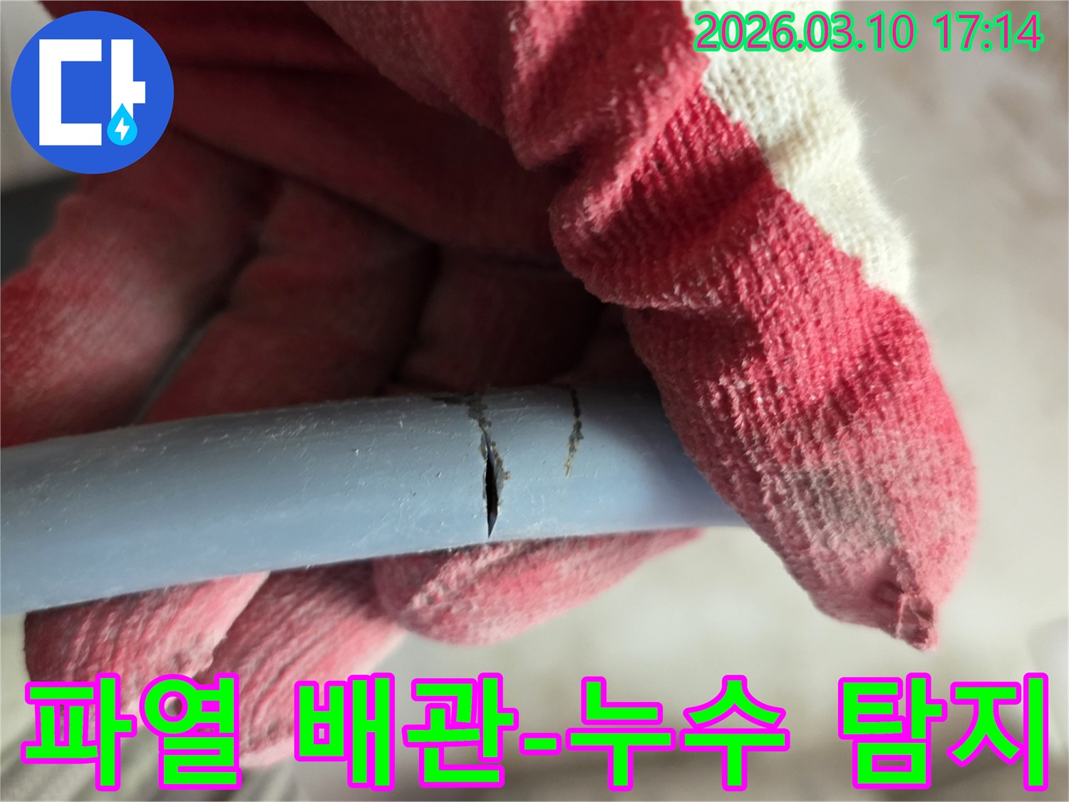 작업용 장갑을 낀 손이-파열된 배관의 손상 부위를 가리키며-누수 지점을 확인하고 있습니다