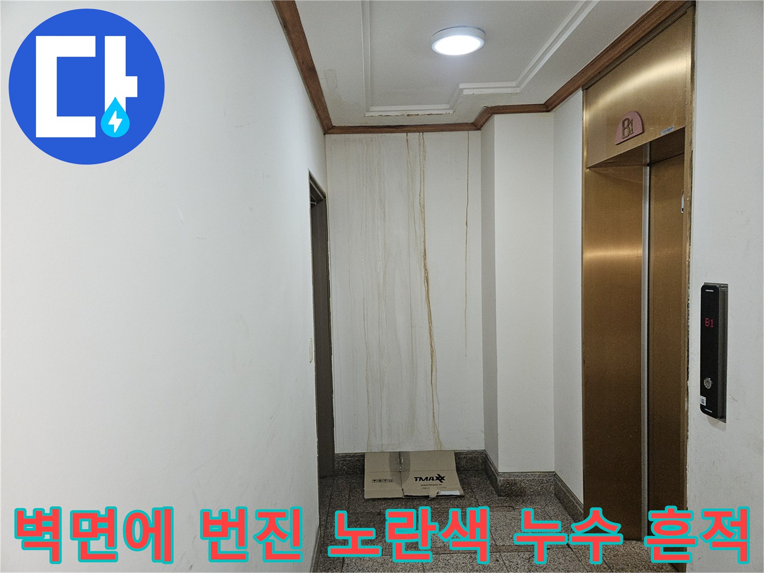엘리베이터 옆 하얀 벽면에 길게 형성된 누수 오염 자국