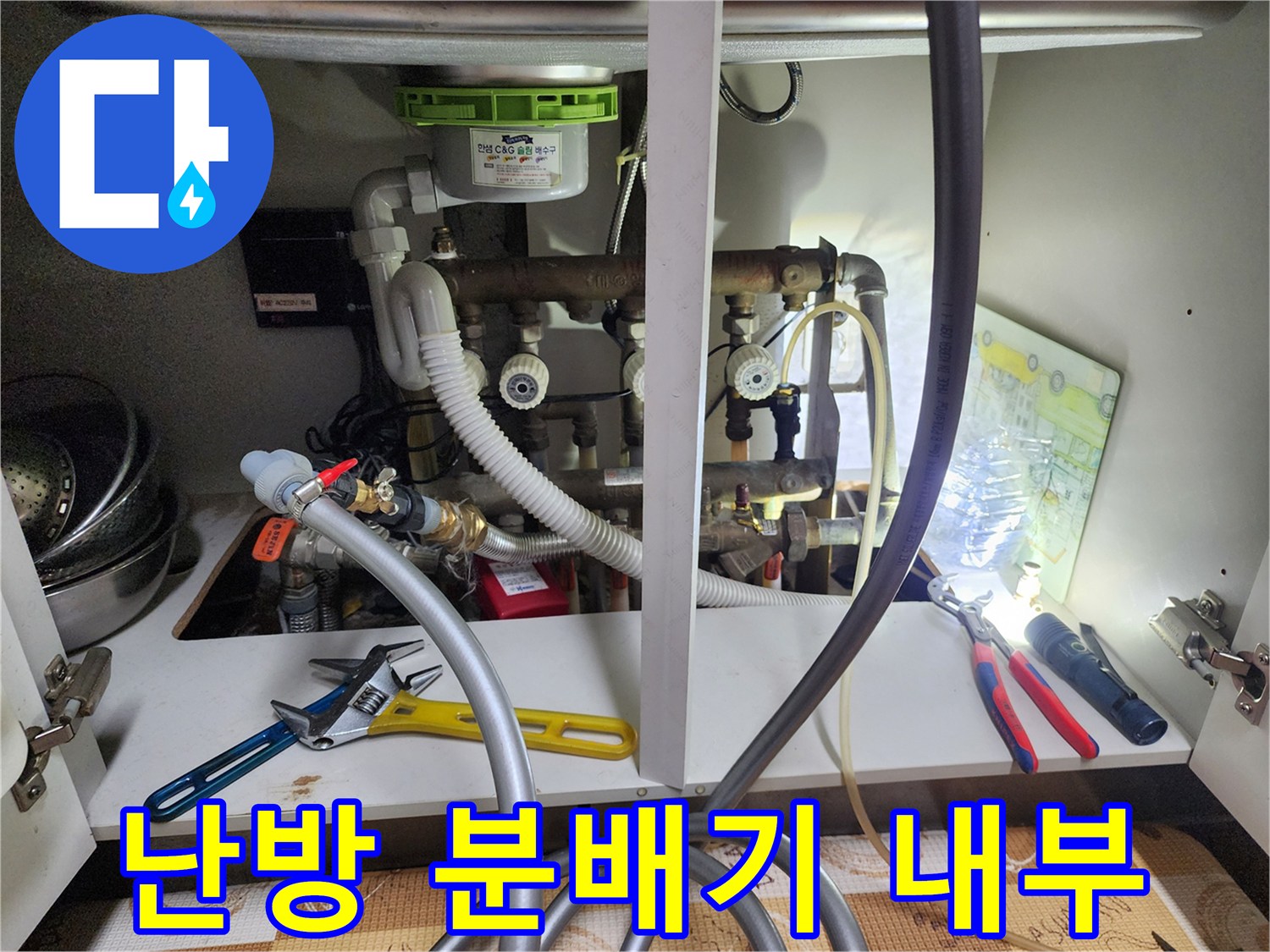 싱크대 밑 공간의 난방 분배기와 밸브 그리고 연결된 배관들의 근접 촬영 이미지입니다.