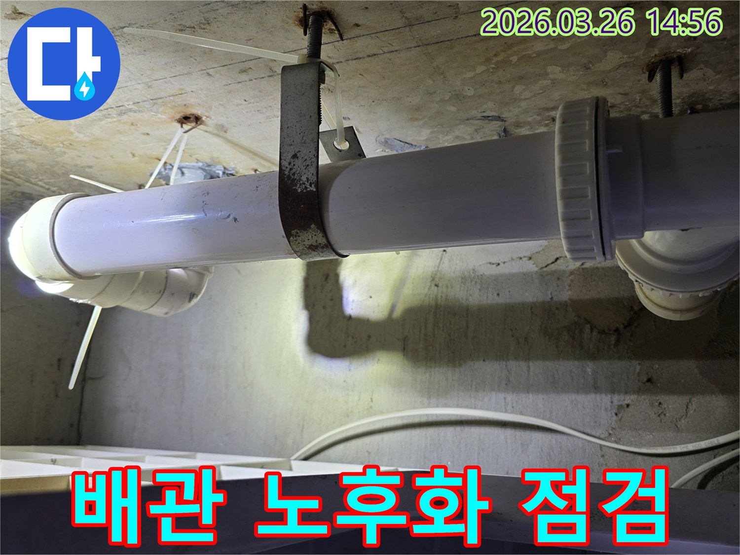 콘크리트 천장에 고정된-오래된 하얀색 배관과-녹슨 금속 지지대의 모습으로-배관 노후화 상태를 보여줍니다