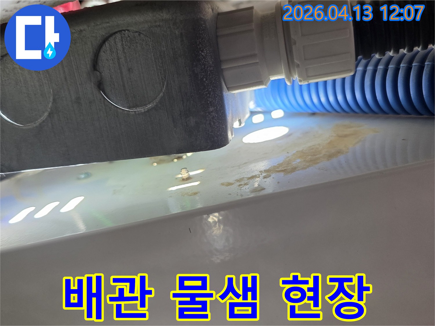 배관 연결 부위에서 물이 새어 나와 주변에 물방울과 얼룩이 생긴 모습입니다-즉각적인 조치가 필요합니다