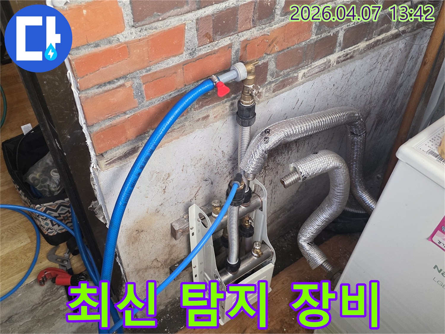 벽돌 벽 옆에-최신 누수 탐지 장비가-설치되어 있으며-파란색 호스가-배관에 연결되어-정확한 누수 지점을 찾기 위한-작업이 진행 중입니다.