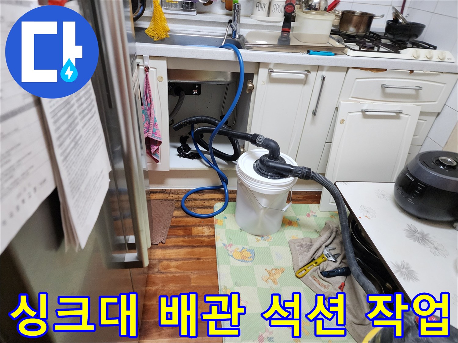 주방 싱크대 아래쪽에서 배관 내부 이물질을 제거하기 위해 석션기를 연결한 모습입니다.