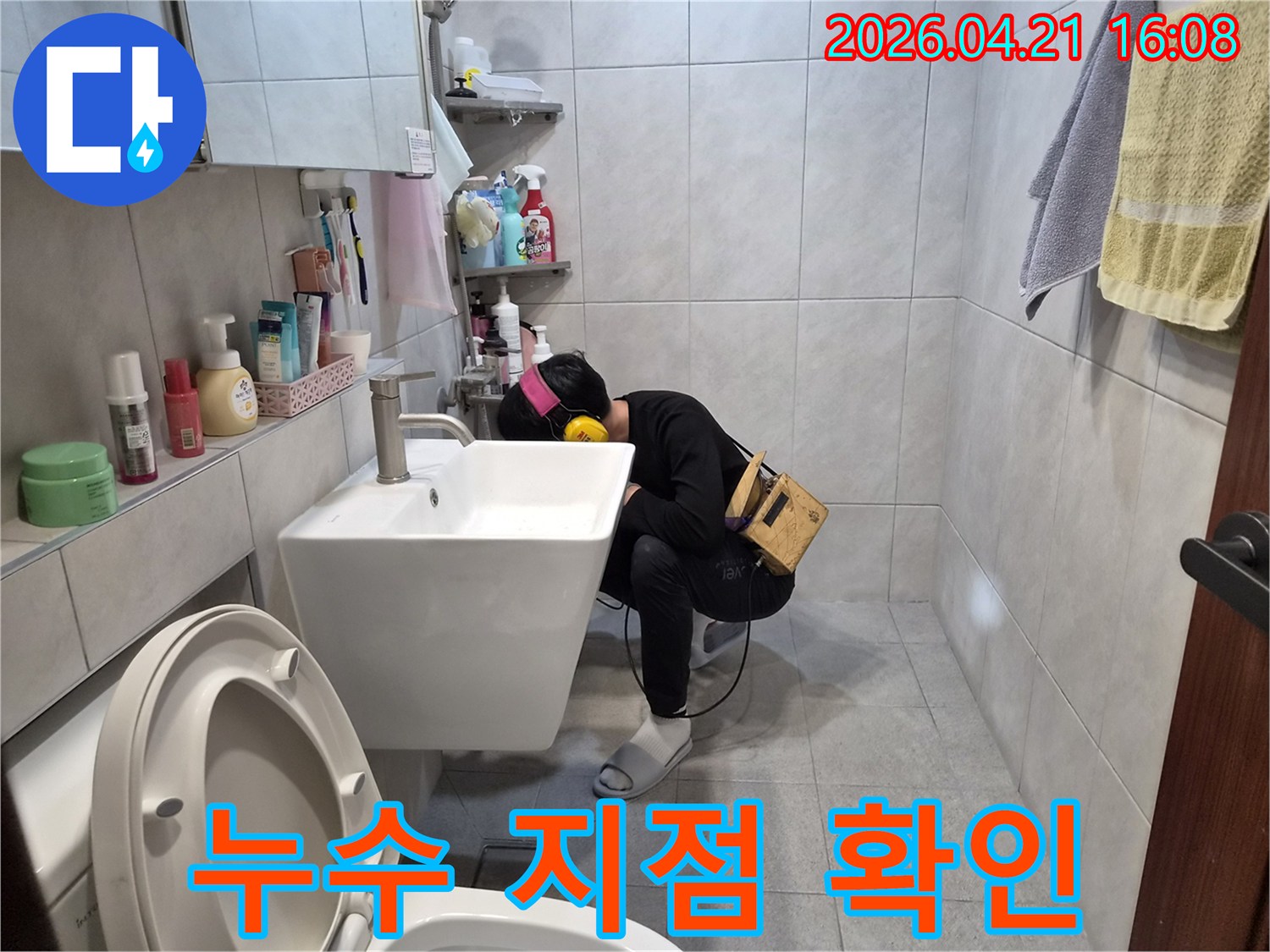 아파트 욕실에서 누수 탐지 전문가가-청음 장비를 이용해-배관의 미세한 누수음을 듣고-정확한 누수 지점을 확인하고 있습니다