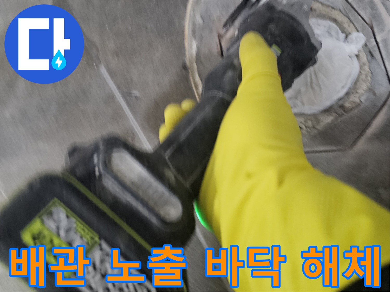 노란색 작업 장갑을 착용한-전문가가-전동 공구로-배관 주변의 바닥 타일을-세심하게 제거하여-배관을 노출시키는 과정입니다.