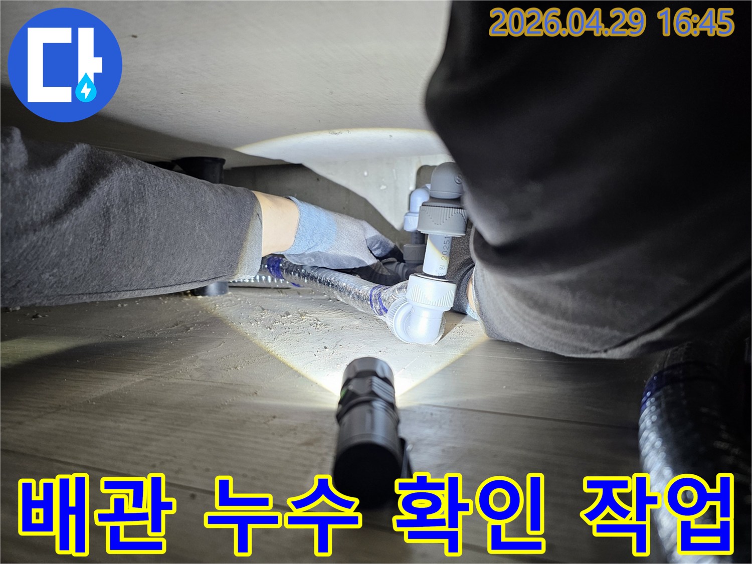 숙련된-기술자가-좁은-공간에서-손전등을-사용하여-배관-누수-여부를-확인하는-장면