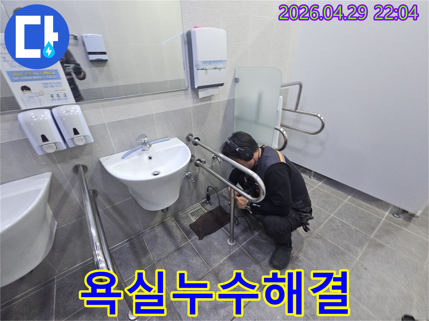 헤드폰을 착용한 기술자가-공용 화장실의 세면대 배관에서-미세한 누수 지점을 찾아내고 있습니다.