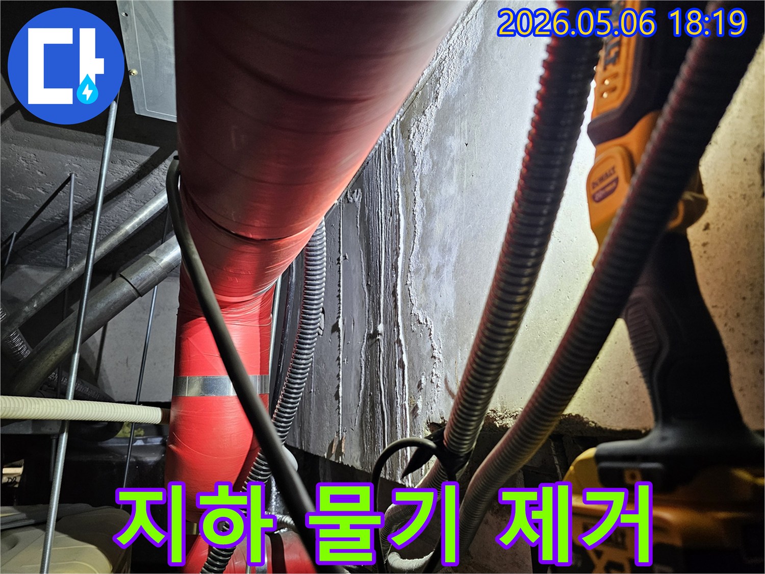 어두운 지하 공간에서-빨간색 배관 옆-습기로-젖은-벽면을-촬영한-사진으로-누수 방지를-위한-물기 제거-및-보강-전-상태를-보여줍니다