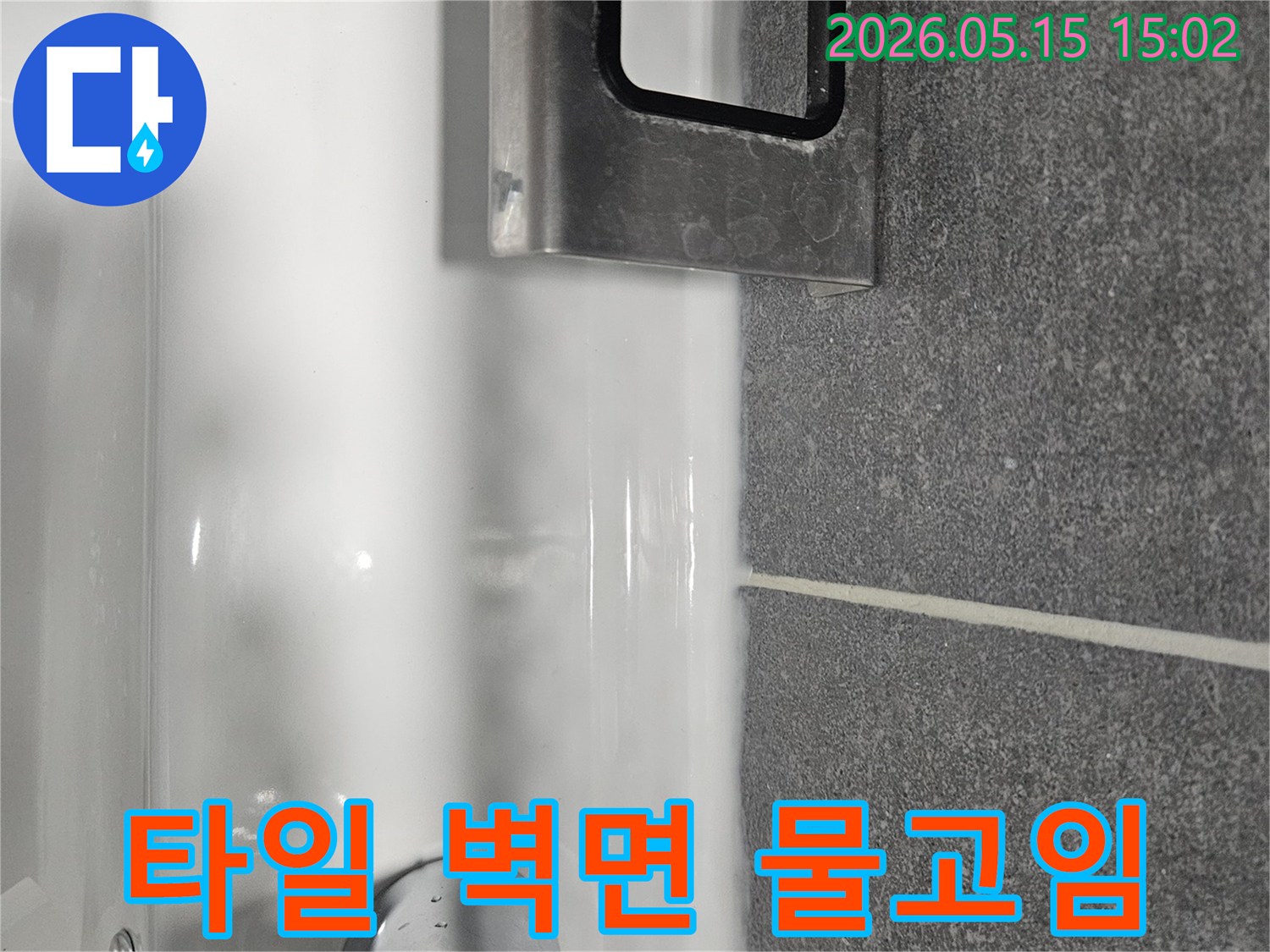어두운 타일 벽면과-하얀 세면대 경계에-물이 고여있는-모습을-보여주는-욕실 사진