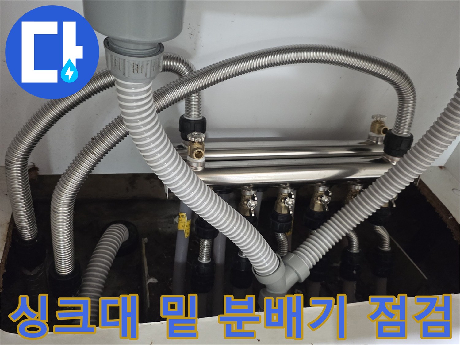 주방 싱크대 내부-분배기와 은색 플렉시블 호스들이 연결된 복잡한 배관 구조를 촬영함