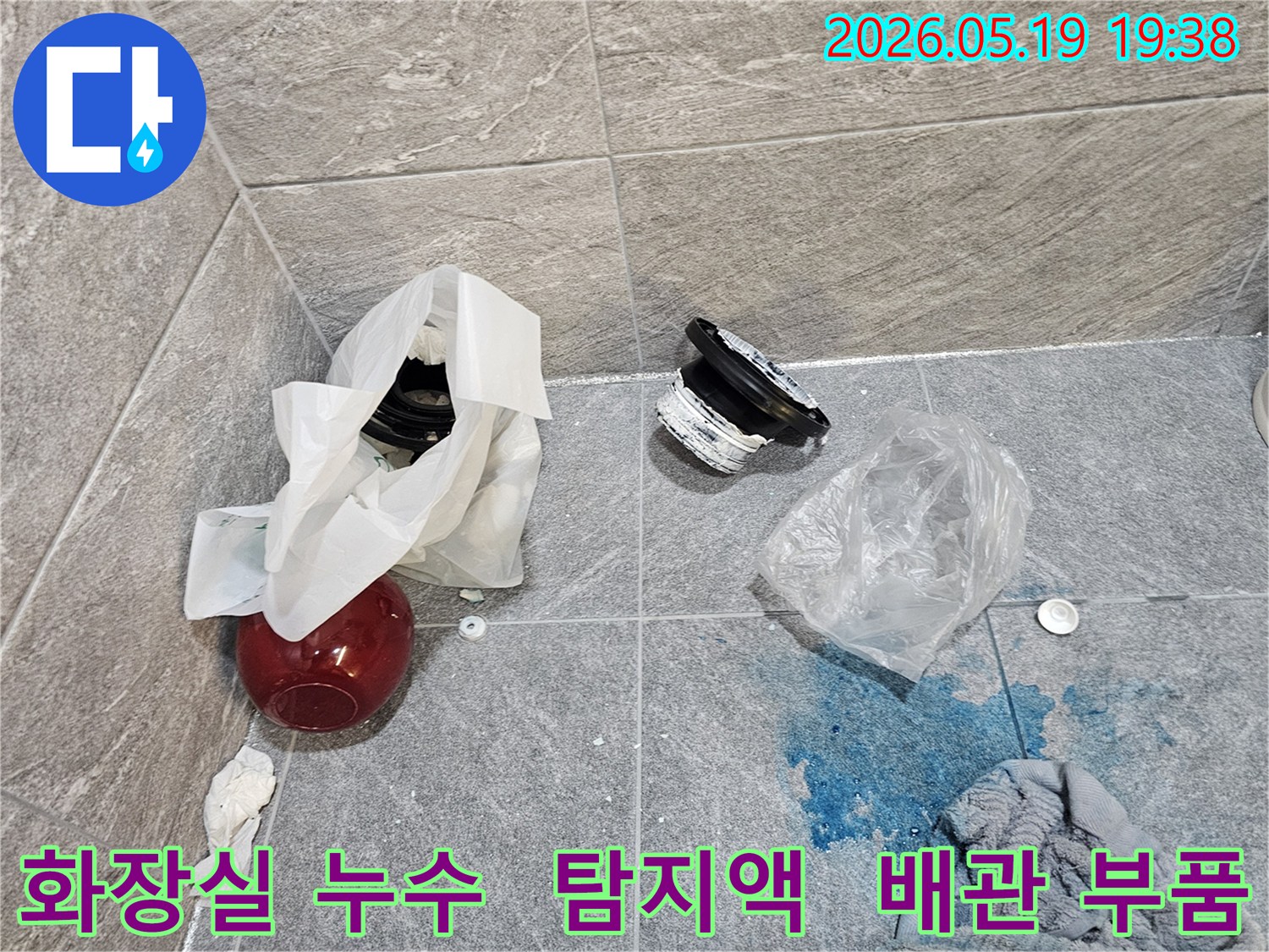 화장실 누수 탐지 현장에서-파란색 탐지액이 누수 지점을 가리키고-주변에는 손상된 배관 부품들이 놓여 있습니다