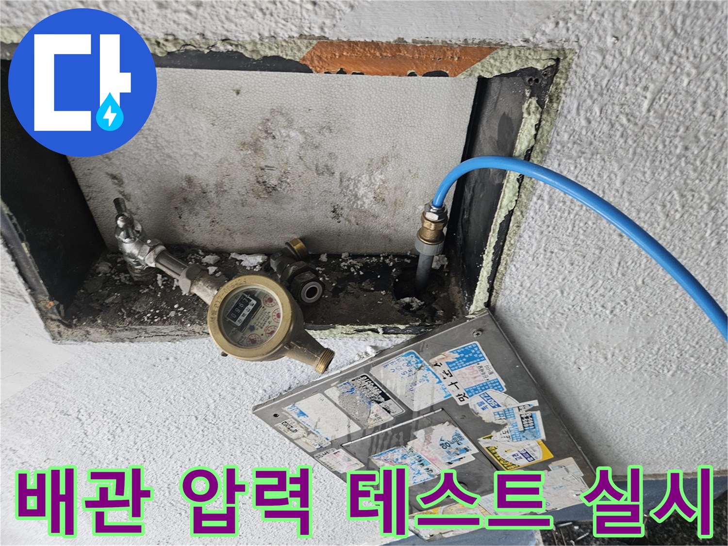 벽면 틈새에 노출된 계량기와 검사용 호스의 모습입니다.