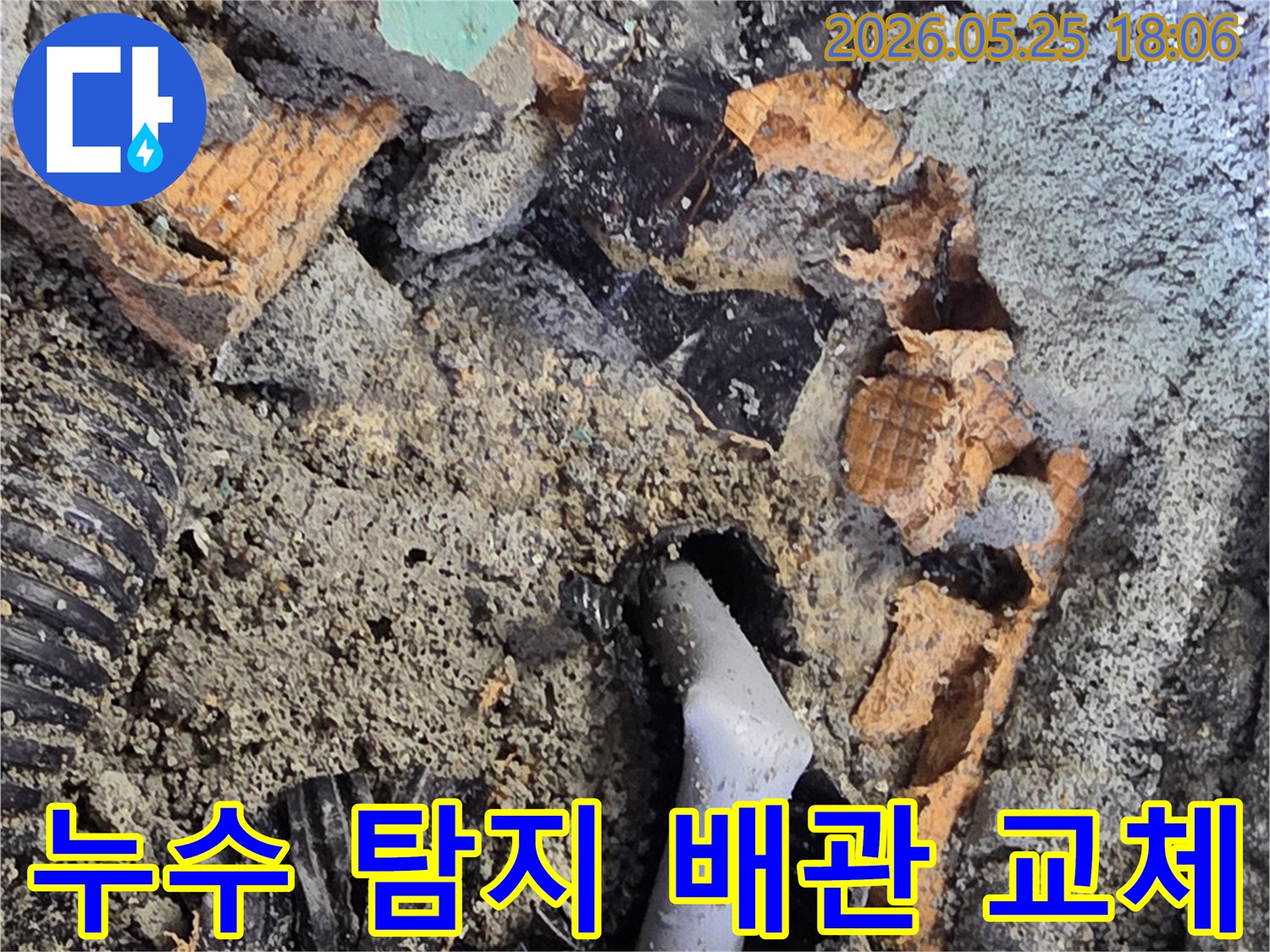 파쇄된 바닥 아래에서 드러난 젖은 배관과 주변의 흙-콘크리트 조각들은-누수 수리를 위한 배관 교체 작업을 보여줍니다.