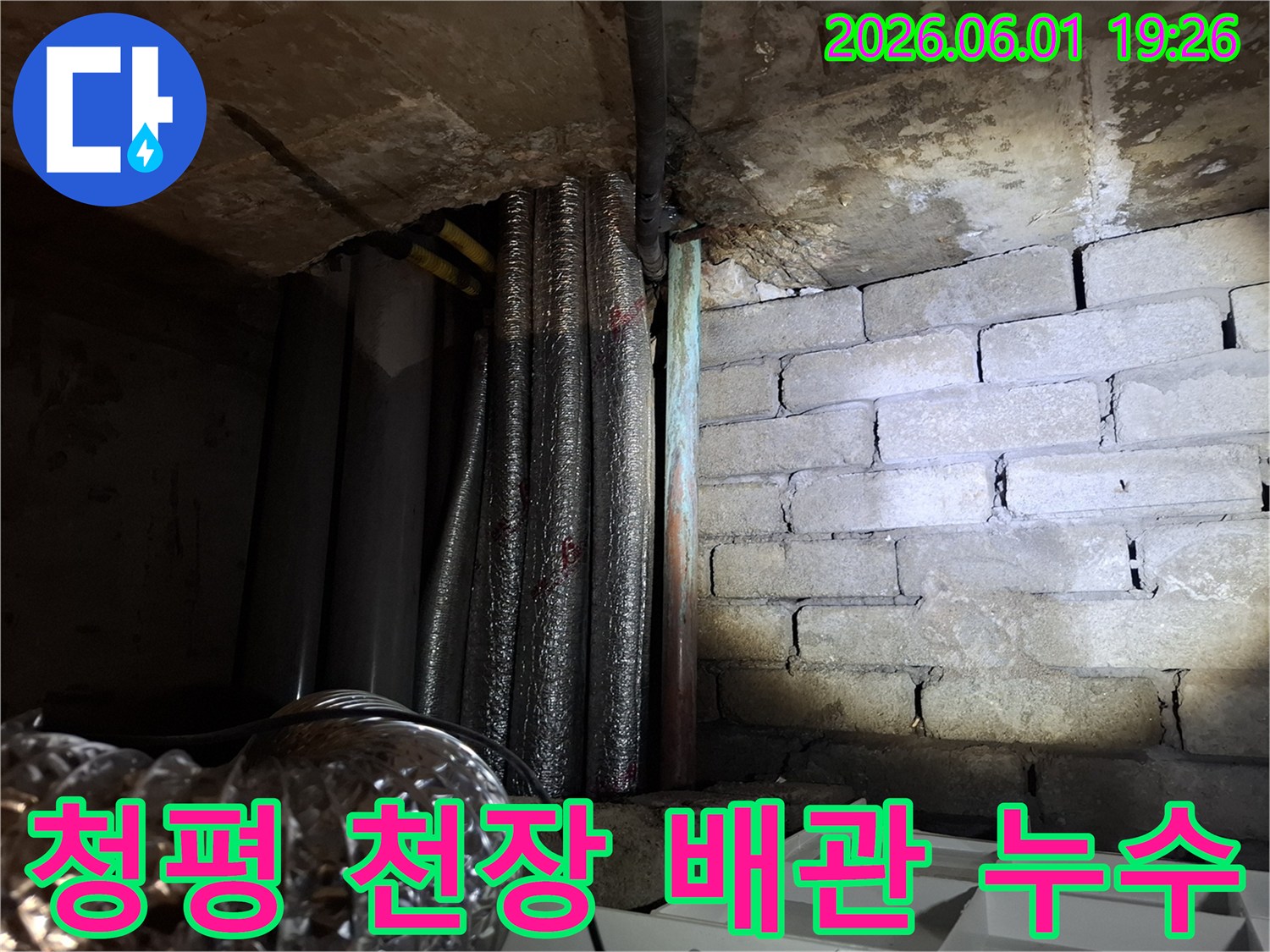 어두운 환경에서-천장 배관 주변의-누수 흔적과-젖은 벽돌 벽면을-보여주는 현장 사진입니다