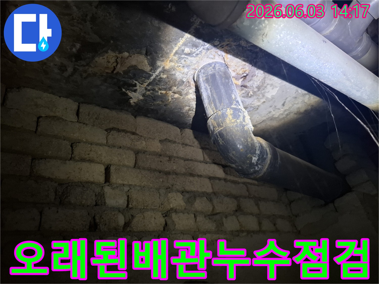 어두운 지하 공간의-낡은 벽돌 벽과-오래된 배관 주변에서-발견된 누수 흔적을-조명으로 비추어-정밀하게 진단하는 모습