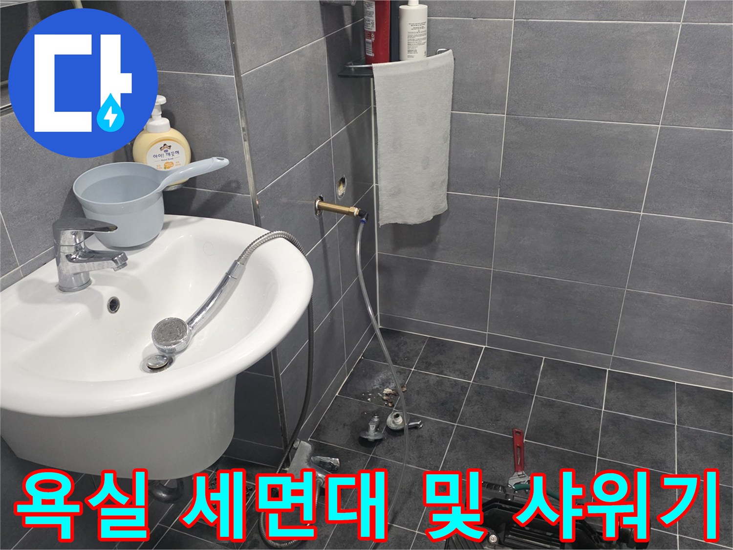 세면대와 샤워기가 설치된 회색 타일 욕실 내부의 모습입니다.