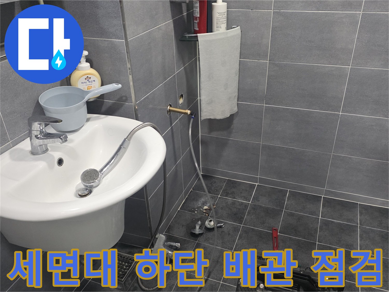 욕실 세면대 밑으로 연결된 은색 금속 배관과 샤워기 호스