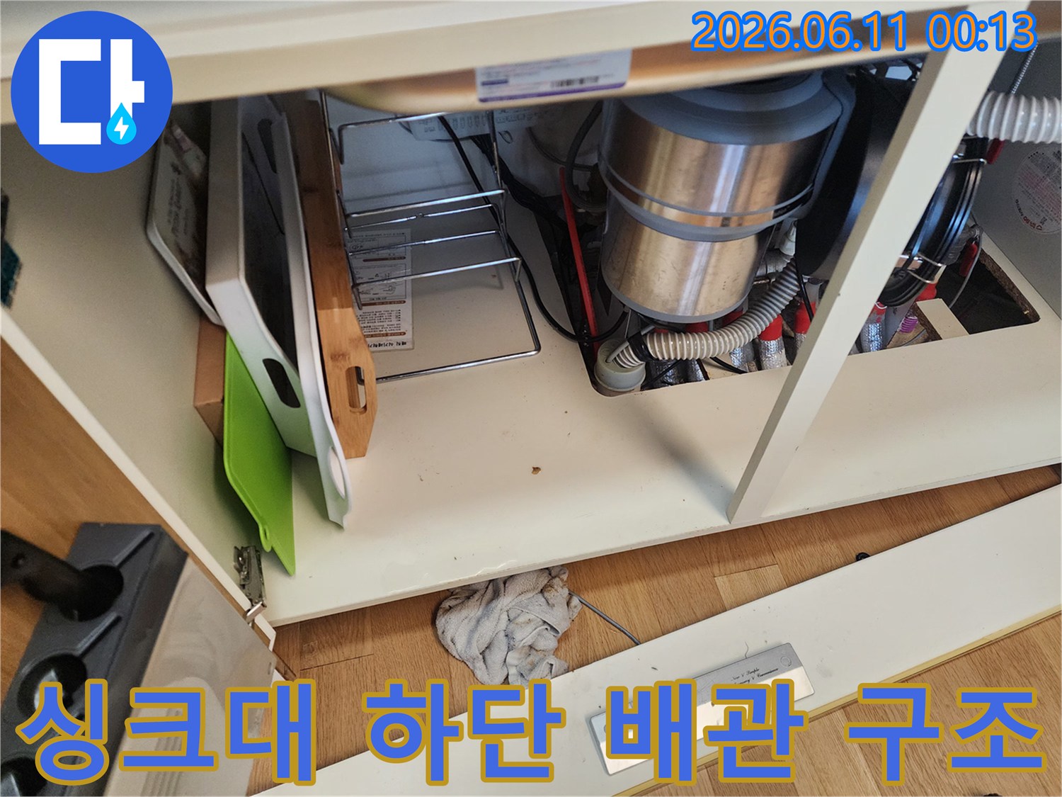 싱크대 밑 공간에 설치된 은색 배관과 흰색 주름관 연결부