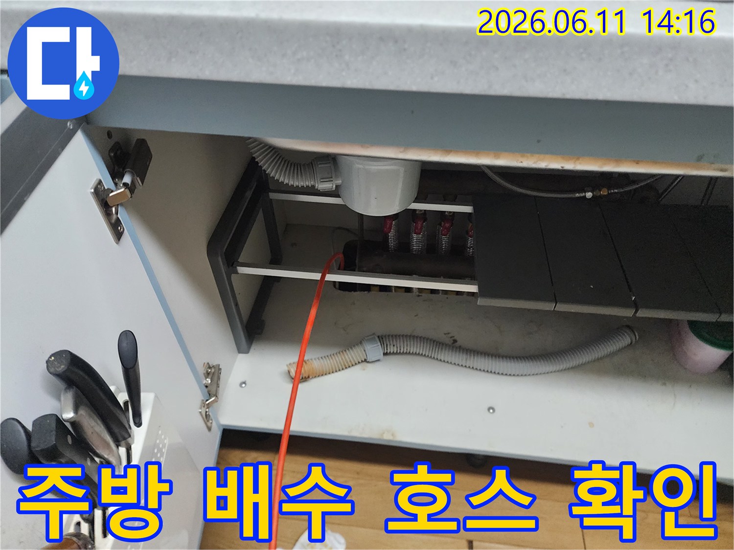하얗고 회색빛이 도는 주름진 배수 호스가 싱크대 하부 배관에 연결되어 있습니다.