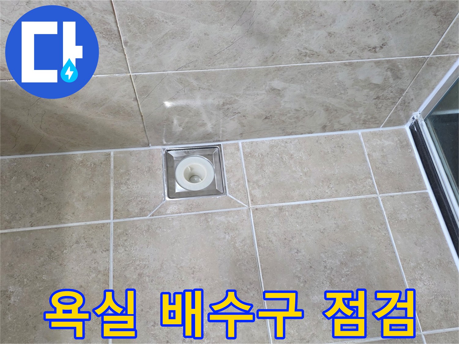깨끗하게 시공된 욕실 타일 중앙에-사각형 배수구가 위치하며-주변 마감 상태를 면밀히 관찰하는 사진입니다