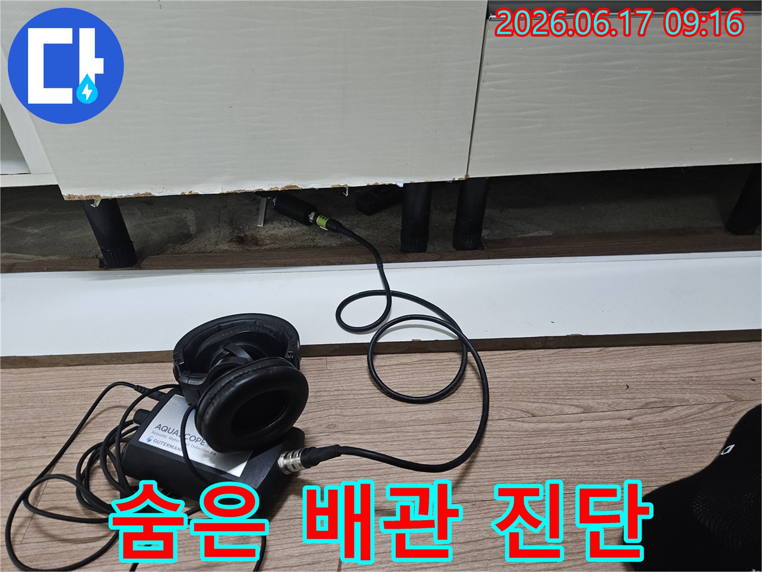 누수 탐지 장비의 센서가-싱크대 하부장 틈새에 삽입되어-숨겨진 배관 누수음을 감지하는 모습