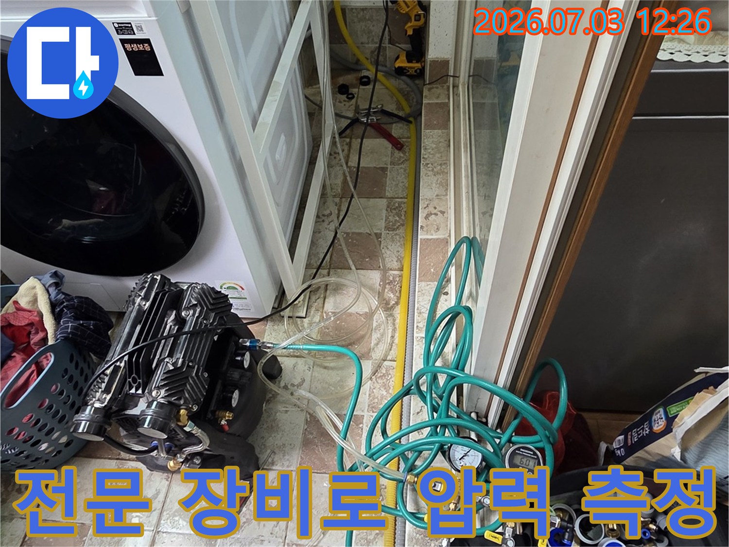 다양한 색상의 호스와 게이지가 연결된 장비로 세탁기 옆 배관을 정밀 점검하는 모습