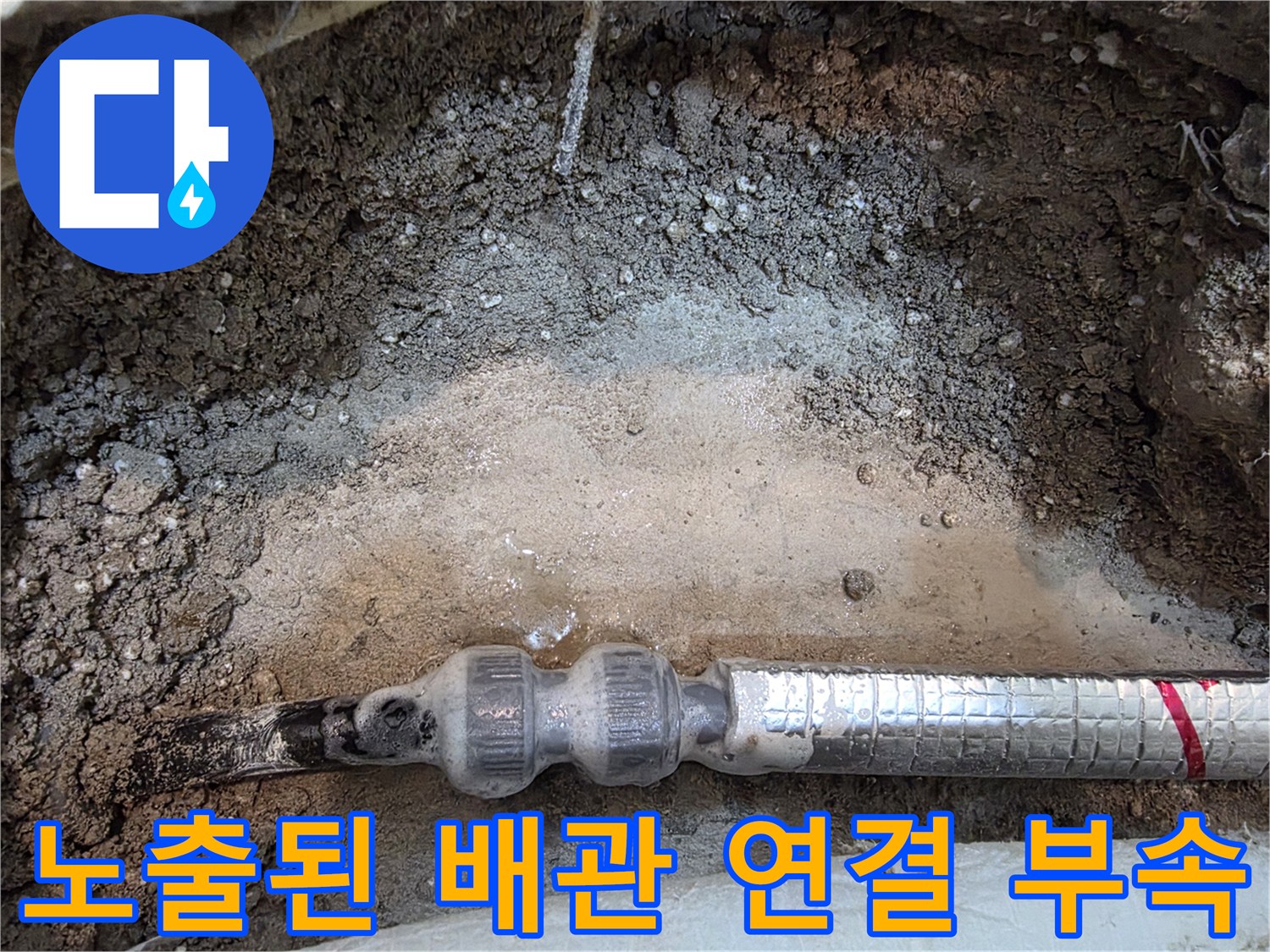 흙과 콘크리트 사이에 노출된 은박 보온재 배관의 모습
