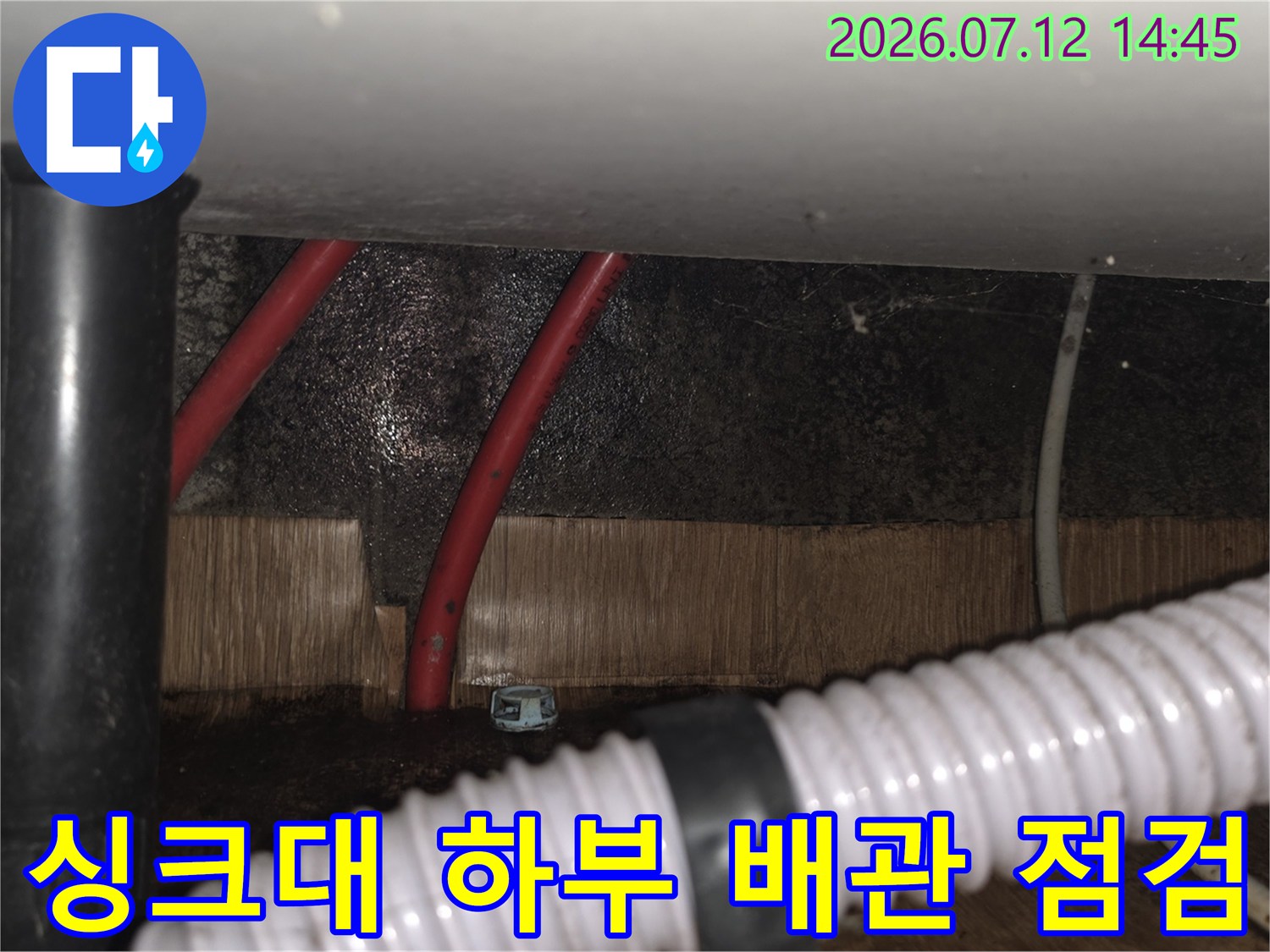 싱크대 아래 위치한 검은색 하수관과 붉은색 배관의 연결 부위를 상세하게 촬영한 사진입니다.