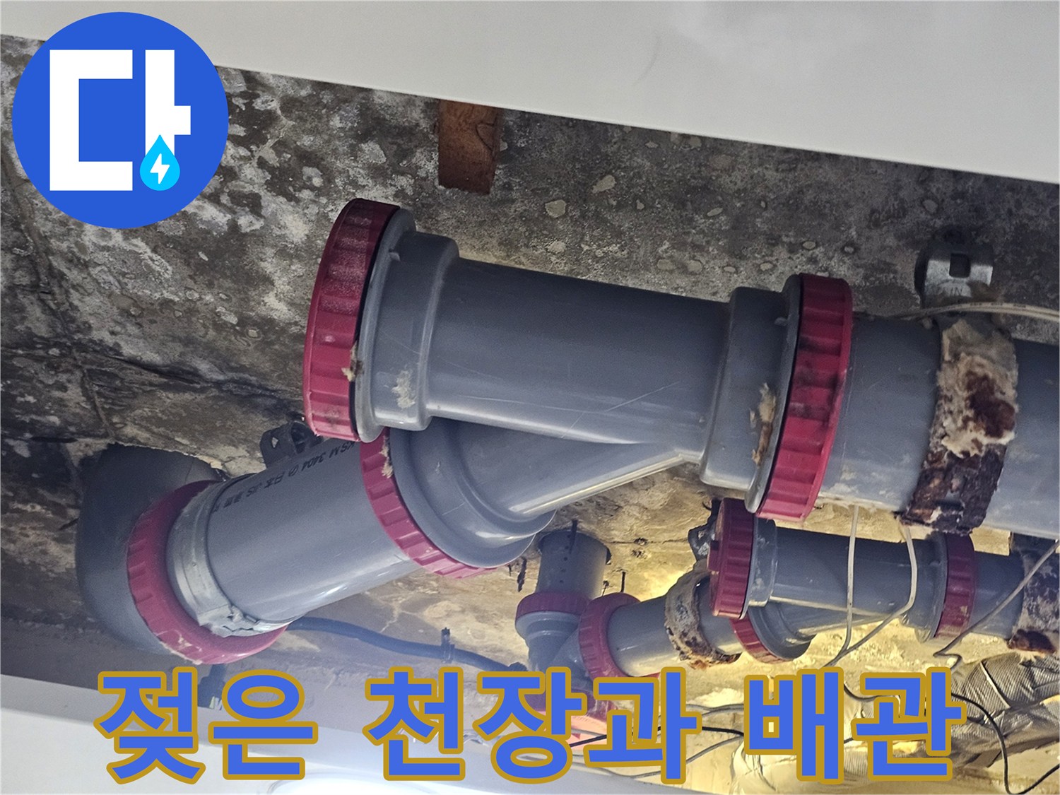 습기로 얼룩진 천장 구조물과 붉은색 마감 부속이 있는 배관