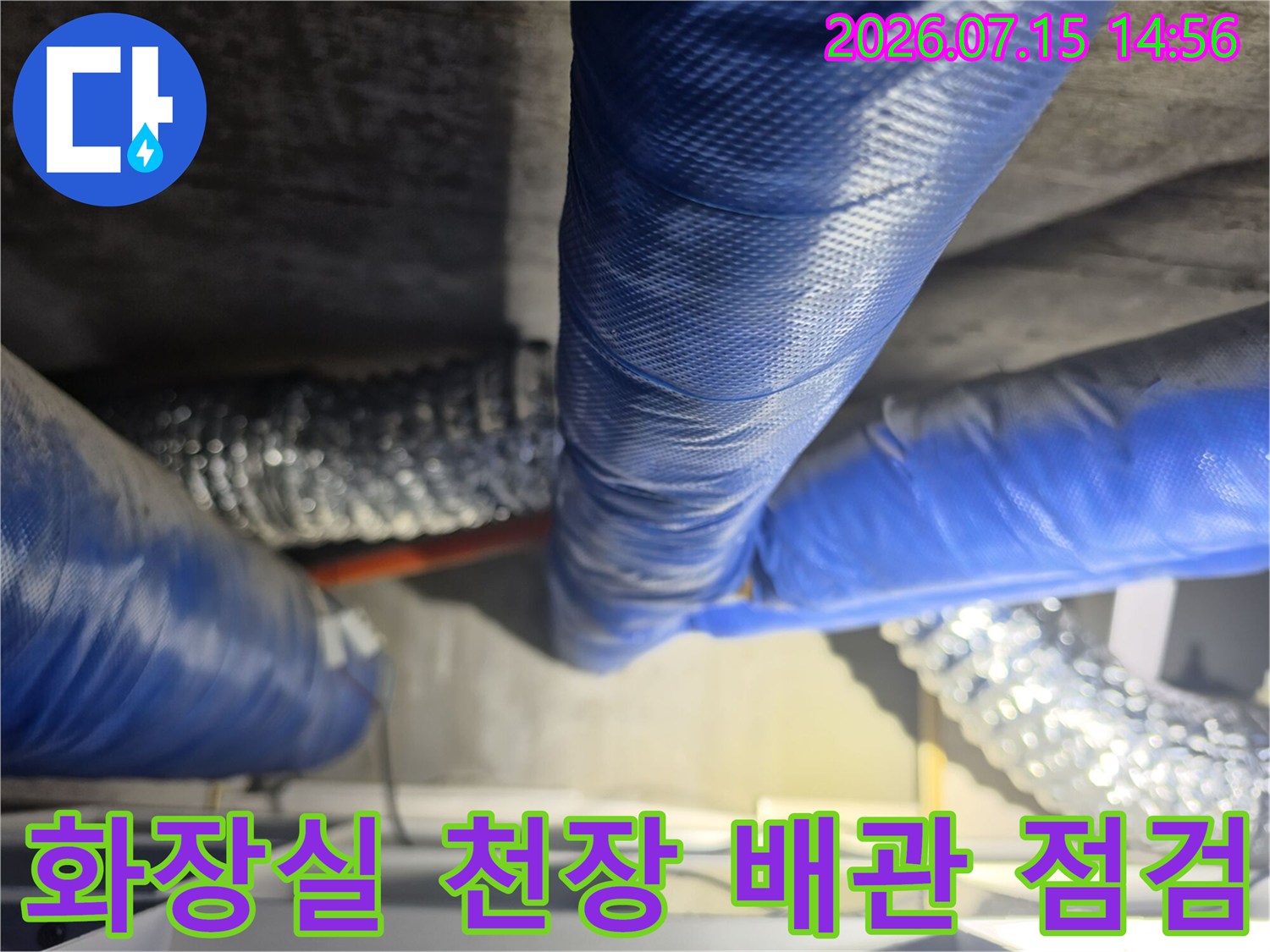 파란색 보온재로 감싸진 화장실 천장 내 배관과 은색 단열재가 덮인 배관 구조물