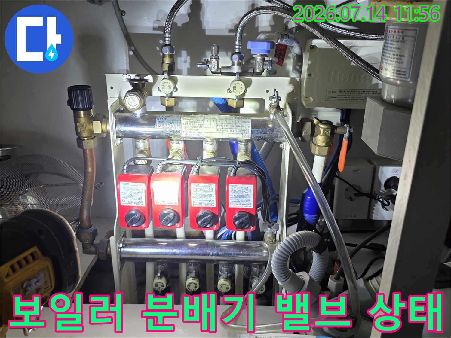흰색 벽면 앞에 설치된-빨간색 손잡이의 보일러 분배기와 금속 배관 연결 부위