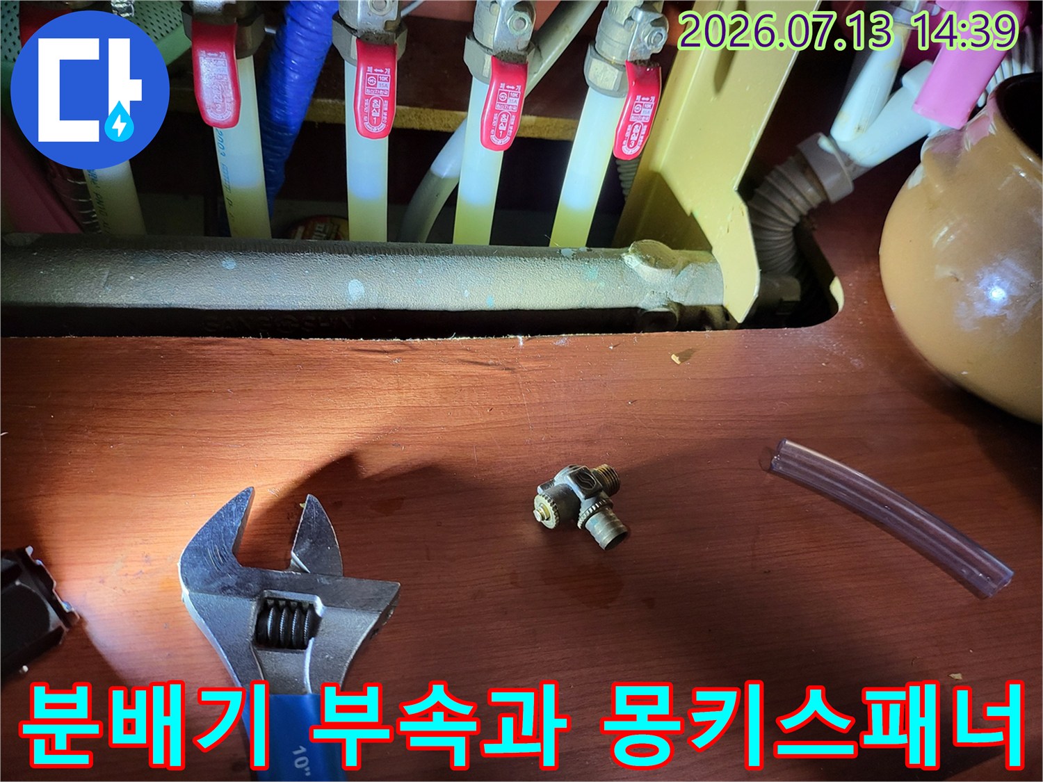 누수 수리를 위해 분리한 금속제 배관 부속-몽키스패너와 투명 호스가 놓여있는 모습